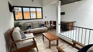 A modern living room with a sofa, coffee table, and chairs. There is a balcony with a railing and a TV mounted on the wall. - Hermosa casa, con Parqueo propio, Ideal para pasar momentos en familia o pareja. (Jocotenango)