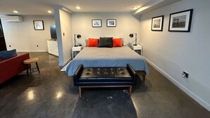 Une chambre à coucher moderne avec un grand lit, des tables de chevet, un fauteuil rouge et une petite table.