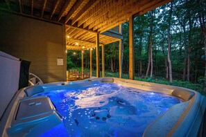A hot tub with a wooden deck and glass walls, surrounded by a forest.
