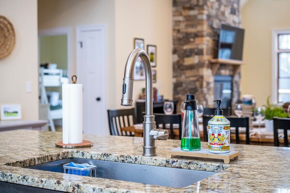 A kitchen with a granite countertop, stainless steel faucet, and a built-in sink. There are two bottles of hand soap and a candle on the counter.