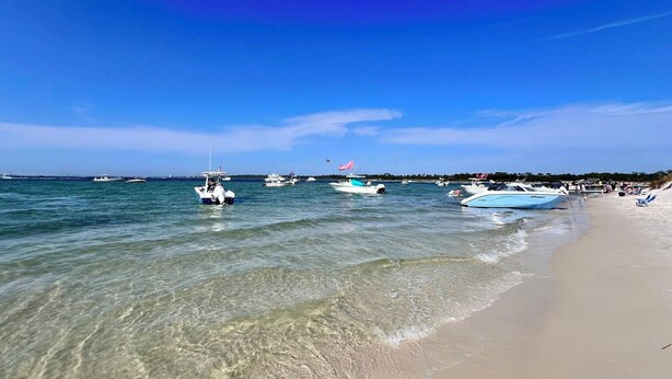 Uma praia com águas cristalinas, barcos e areal arenoso.