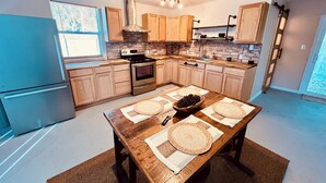 Cozinha moderna com armários de madeira, geladeira de aço inoxidável, forno embutido e mesa de jantar com jogos americanos.