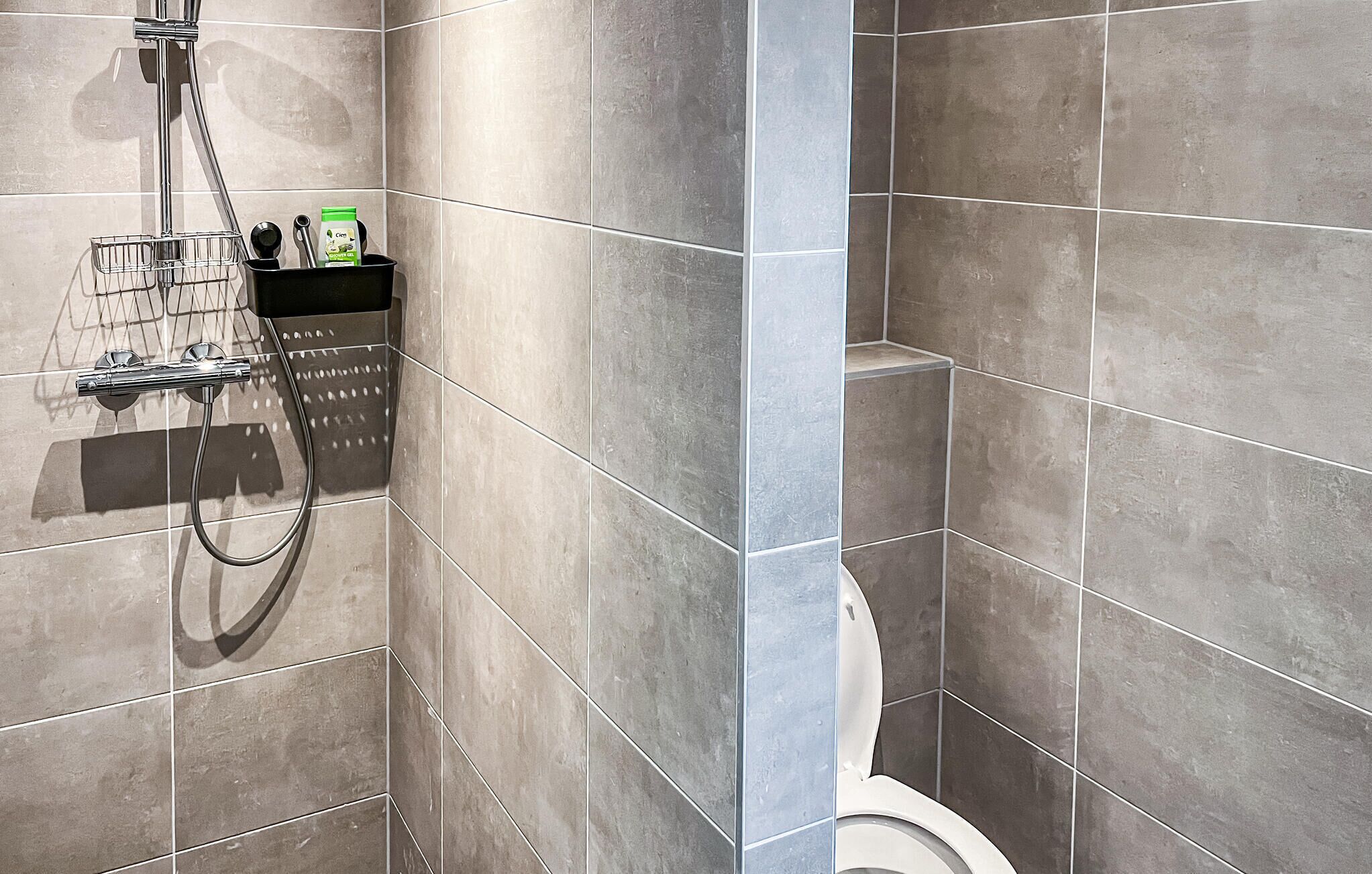 A modern bathroom with grey tiles, a shower, and a toilet.