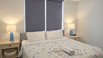 Une chambre d’hôtel avec un lit, deux tables de chevet, une fenêtre avec des rideaux et un luminaire suspendu.
