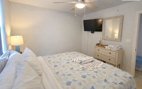 Une chambre à coucher comprenant un lit, une commode, un téléviseur et un ventilateur de plafond.