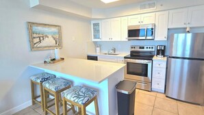 Una cocina moderna con armarios blancos, electrodomésticos de acero inoxidable y una isla central con taburetes de bar.
