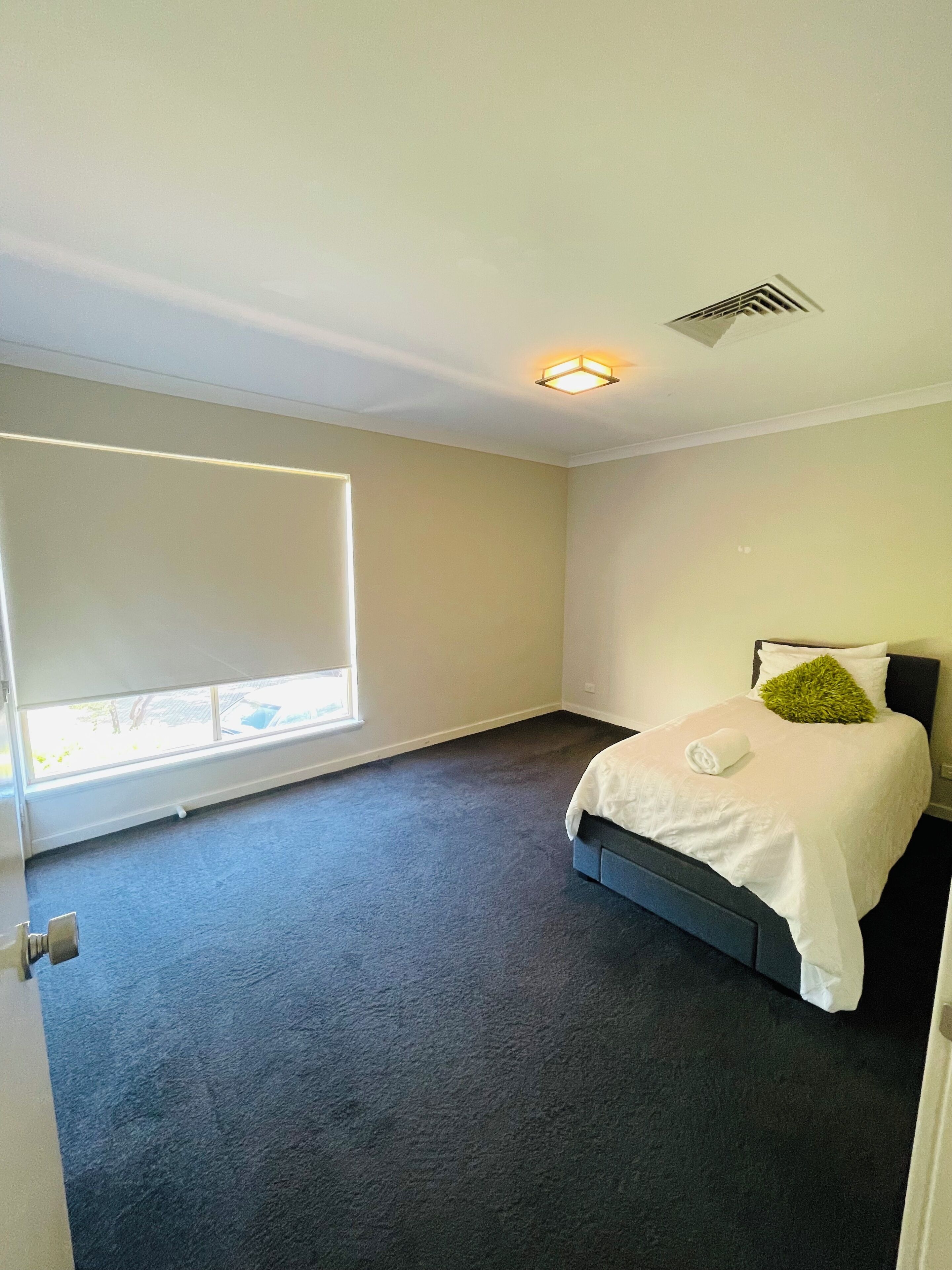 A bedroom with a large window, a bed with white bedding, and a dark carpet.
