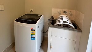 A compact laundry room with a front-loading washer and dryer, a sink with a drying rack, and a cabinet. - Rehoboth homes (The Vines)
