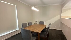 A conference room with a wooden table and six grey chairs, a ceiling light fixture, and a window with blinds. - Rehoboth homes (The Vines)