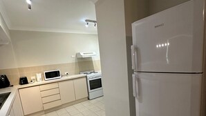 A modern kitchen with white appliances, including a refrigerator, stove, and microwave. - Rehoboth homes (The Vines)