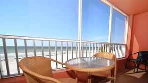 Un balcon avec des fauteuils en osier et une table en verre donnant sur une plage.
