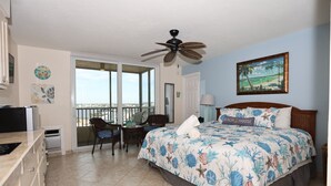 A bedroom with a bed, a ceiling fan, a window with a view, a desk, and a chair.