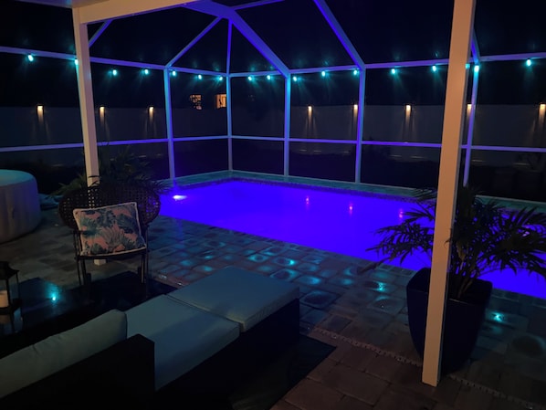 A covered outdoor swimming pool with blue lighting, surrounded by seating and potted plants.
