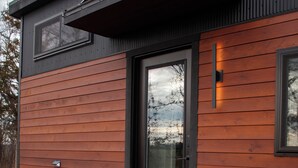 A modern building with a wooden exterior, a black door, and a set of wooden steps leading to the entrance.