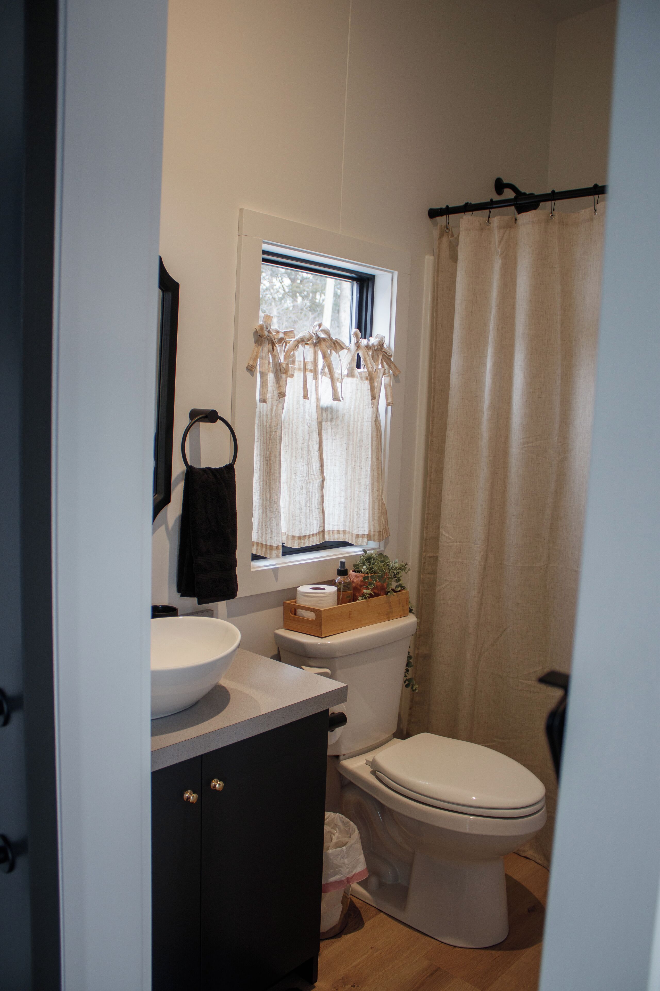 Un baño con lavamanos blanco, inodoro y ventana con cortinas.