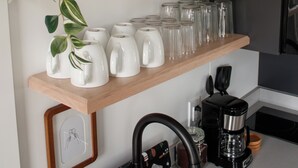 A kitchen with wooden shelves holding white mugs, glasses, and a coffee maker.