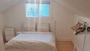 A bedroom with a bed, a nightstand, a window, and a clothing rack. - Home away from home (Vancouver)