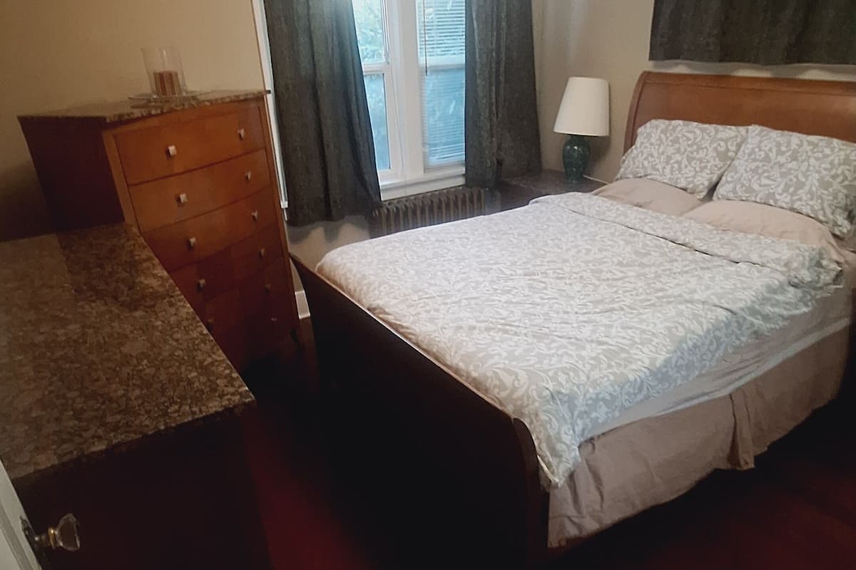 A bedroom with a bed, dresser, and a window with curtains.