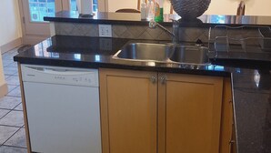 A kitchen with a dishwasher, wooden cabinets, a sink, and a window with curtains. - Home away from home (Vancouver)