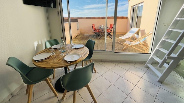 A dining area with a round table, green chairs, and a TV mounted on the wall.