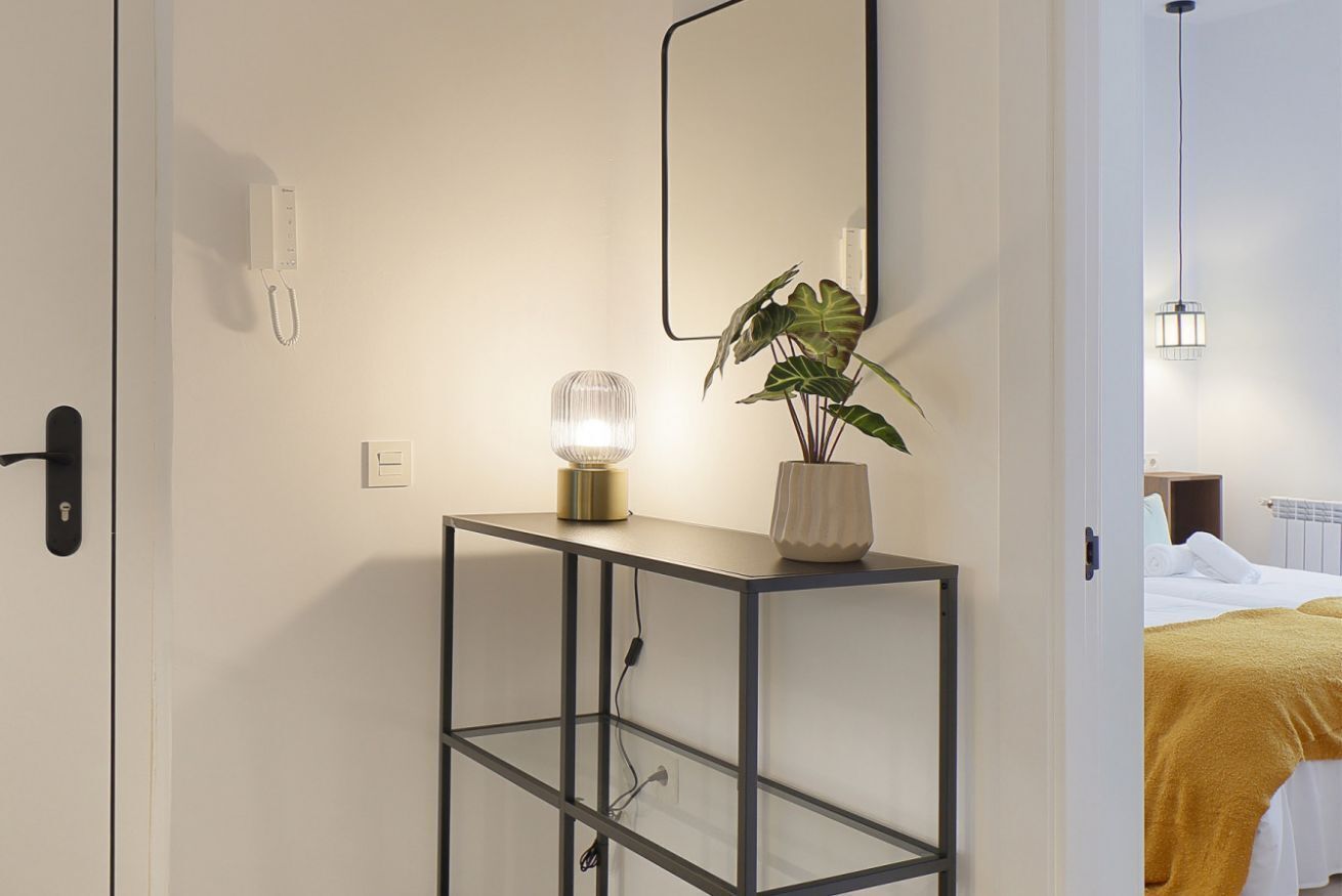 Een hotelkamer met nachtkastje, bedlamp, kamerplant, een bed met een gele deken en een nachtkastje met lamp.