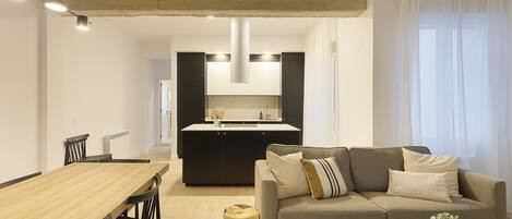 A modern living room with a wooden dining table, a sofa, and a glass coffee table.