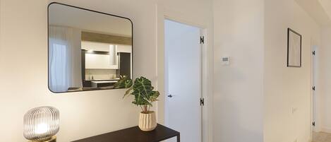 A hallway with a dark console table, a potted plant, a mirror, and a white door.