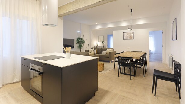 Eine moderne Küche mit Kochinsel, ein Essbereich mit Holztisch und Stühlen sowie ein Wohnbereich mit Sofa und Lampe.