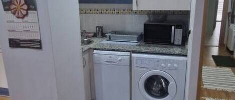 Una cocina compacta con lavadora, microondas y una pequeña encimera.