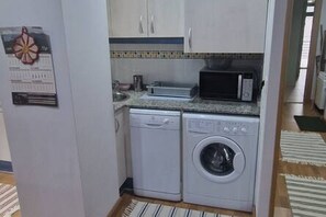 Una cocina compacta con lavadora, microondas y una pequeña encimera.