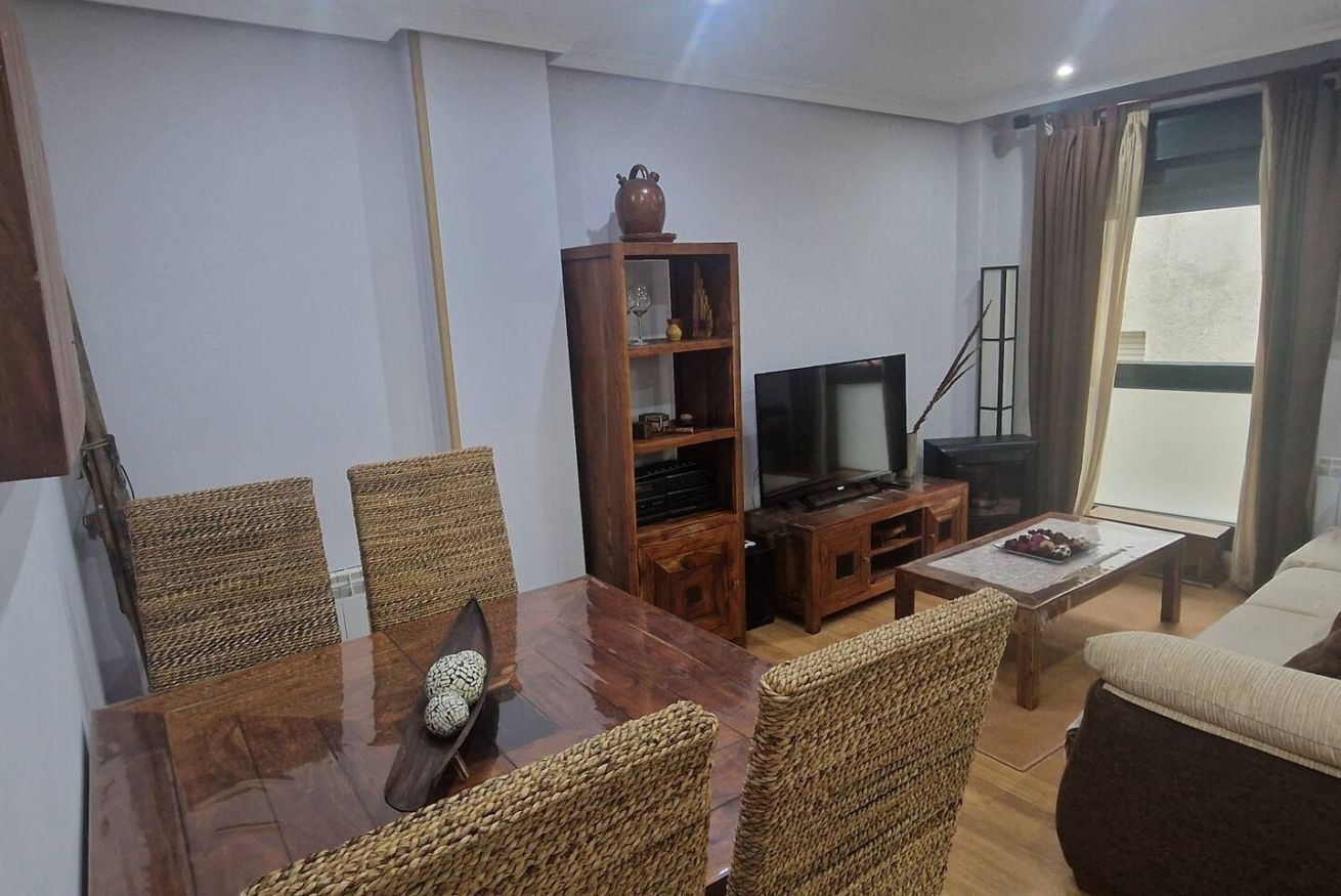 Una sala de estar con una mesa de comedor de madera, sillas de mimbre, un televisor, una estantería y un sofá.