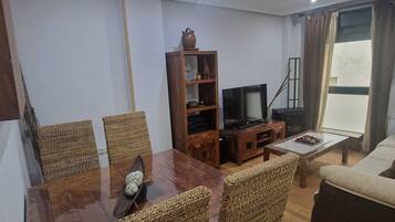 Una sala de estar con una mesa de comedor de madera, sillas de mimbre, un televisor, una estantería y un sofá.