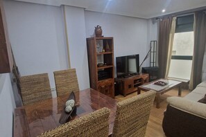 Una sala de estar con una mesa de comedor de madera, sillas de mimbre, un televisor, una estantería y un sofá.