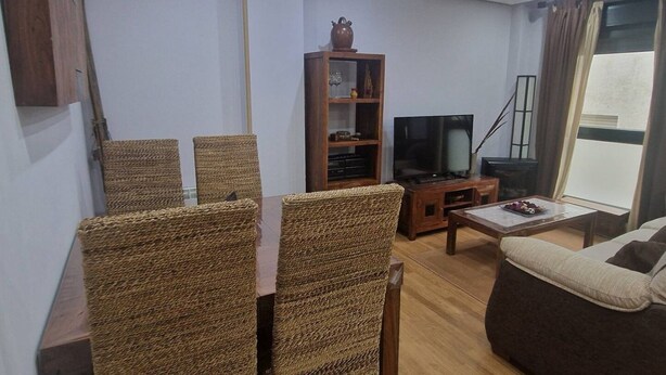 Una sala de estar con una mesa de comedor, sillas de mimbre, un sofá, un televisor y una estantería.