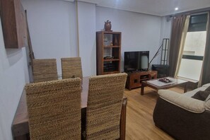 Una sala de estar con una mesa de comedor, sillas de mimbre, un sofá, un televisor y una estantería.