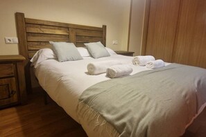 Un lit bien fait, avec une tête de lit en bois, deux oreillers et des serviettes enroulées posées sur le côté.