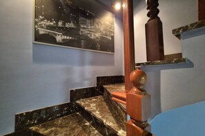 Un escalier avec des marches en marbre et une balustrade en bois, une photographie en noir et blanc accrochée au mur, et un mur bleu.