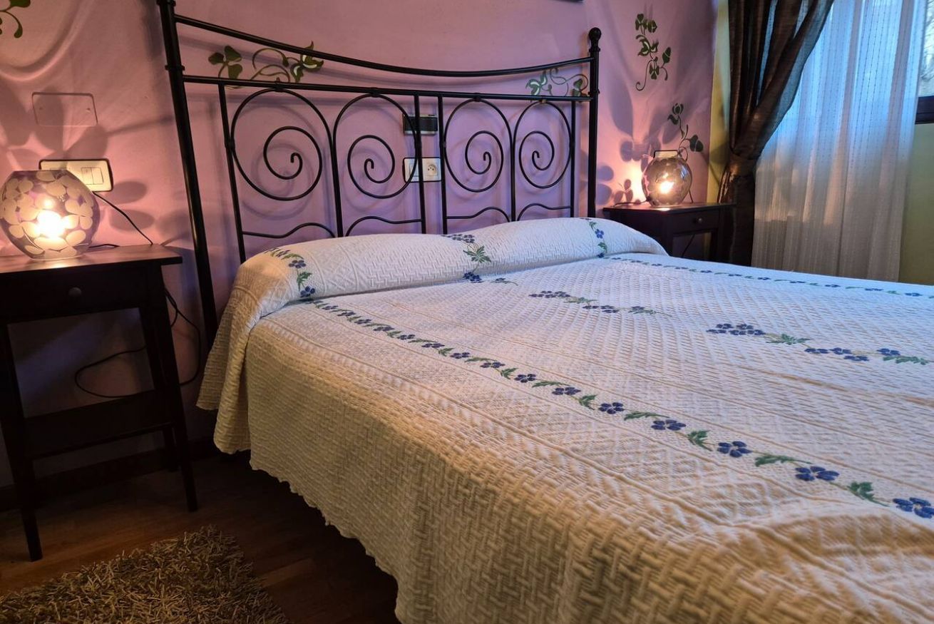 Una cama con colcha de estampado floral, cabecero de metal, mesitas de noche con lámparas y una alfombra pequeña en el suelo.