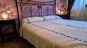 Una cama con colcha de estampado floral, cabecero de metal, mesitas de noche con lámparas y una alfombra pequeña en el suelo.