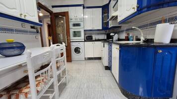Una cocina con alacenas blancas y azules, una lavadora y un comedor con una mesa y sillas blancas.