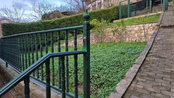 A green metal staircase with a stone wall and a hedge in the background.
