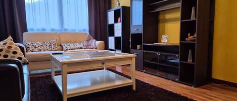 A living room with a sofa, coffee table, and a black shelving unit against a yellow wall.