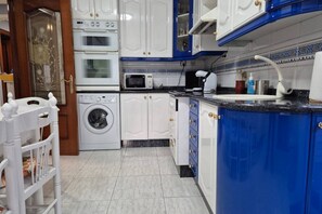 Een keuken met witte en blauwe kastjes, een wasmachine, een magnetron en een spoelbak.