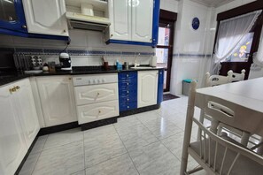 Una cocina con armarios blancos y azules, una estufa y un comedor con una mesa y una silla blancos.