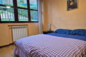 Une chambre avec une couvre-lit à carreaux, un radiateur, une table de chevet avec une lampe et un tableau accroché au mur.