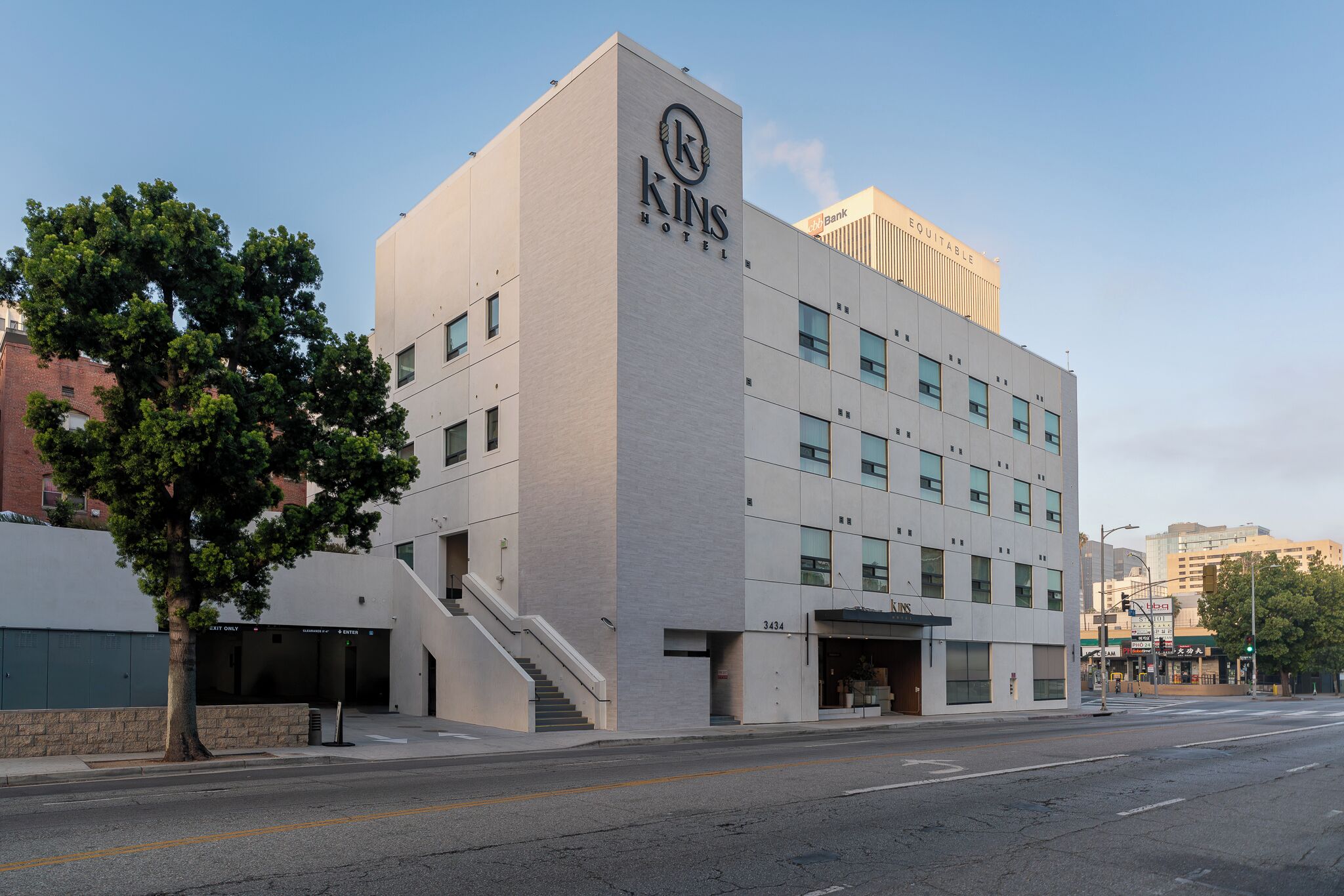 Un hotel moderno con un llamativo letrero que dice 'KINS HOTEL', una escalera que conduce a la entrada y una vista despejada de la calle.