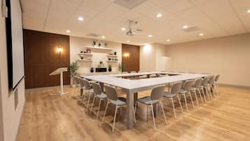 A conference room with a long table, chairs, a podium, and shelves with plants.