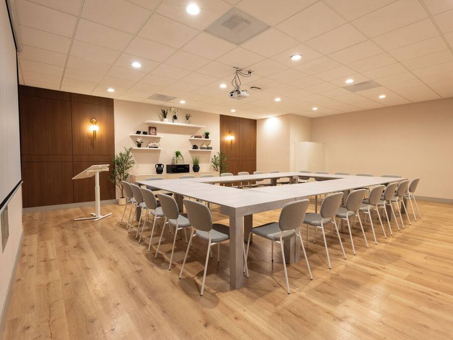 A conference room with a long table, chairs, a podium, and shelves with plants.