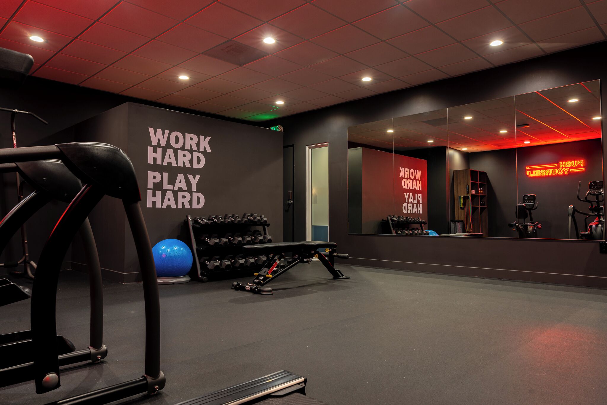 Een fitnessruimte met loopbanden, gewichten en een spiegelwand.