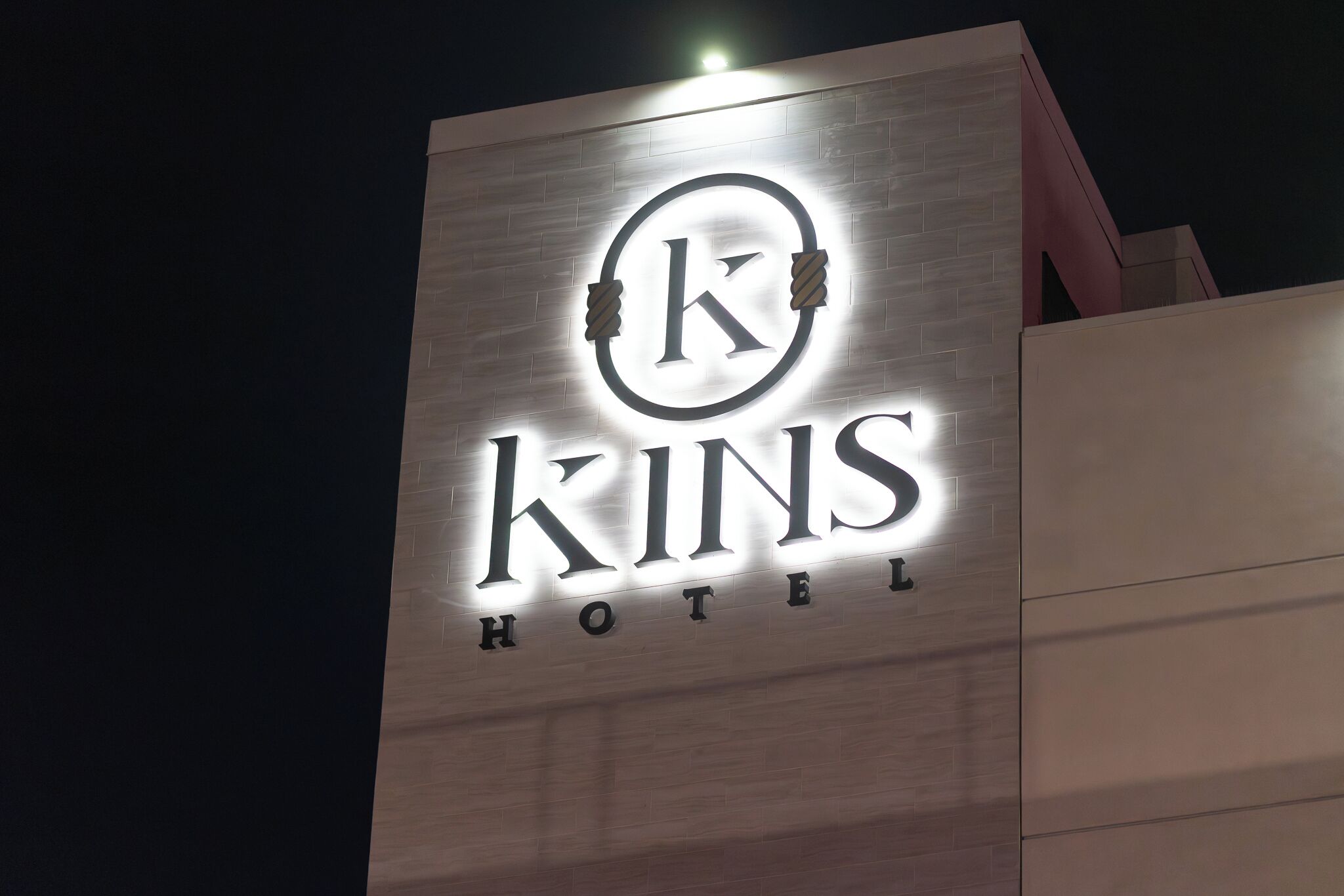 A hotel sign with the name 'KINS HOTEL' illuminated against a night sky.